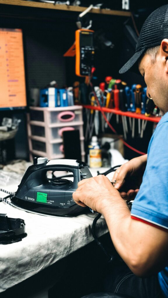pexels-photo-32391510-32391510 Technician in workshop repairing an electric iron with tools and equipment in the background.