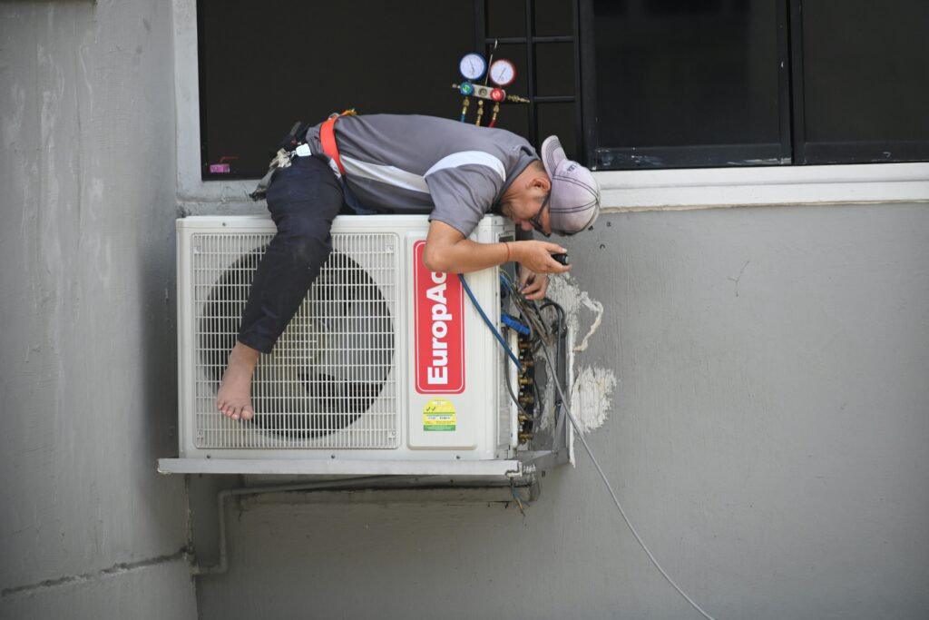 pexels-photo-7347538-7347538 A technician skillfully repairing an outdoor air conditioning unit mounted on a building wall.